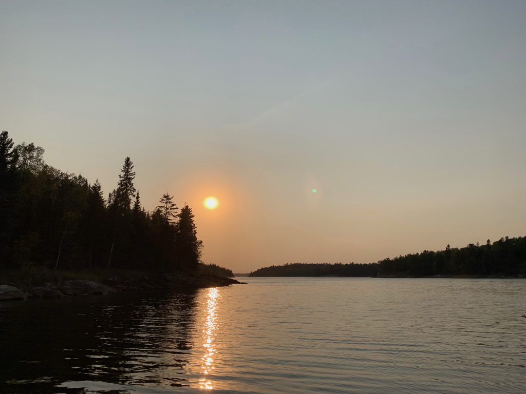 Dusk sun over a river with trees on the shoreline. 